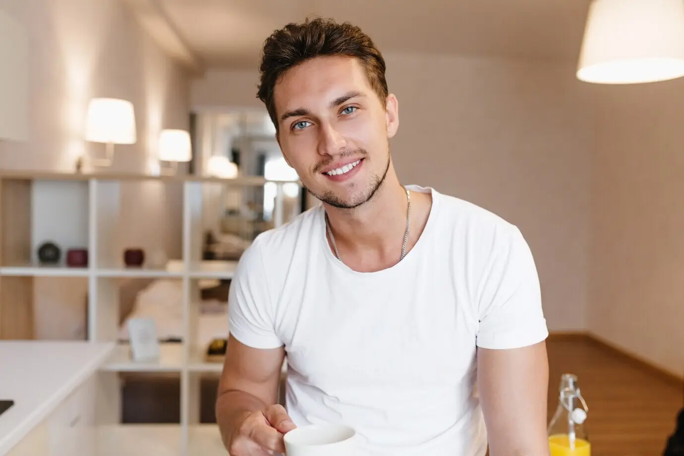 Innenporträt eines zufriedenen, braunhaarigen Mannes mit Bart, der in seiner Wohnung mit einer Tasse Tee posiert.